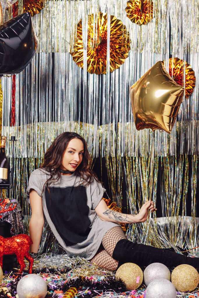 Glamorous woman with a golden balloon star in her hand sitting in a shimmery party space with golden and silver decorations on background. Girl like to party